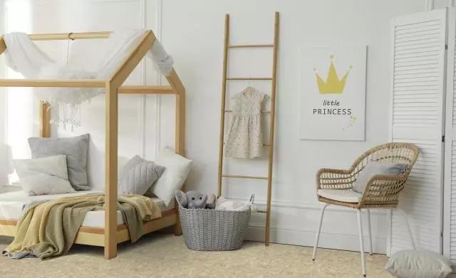 a light childrens room with white walls and wood furniture. A bed shaped like a house on the left and a chair on the right